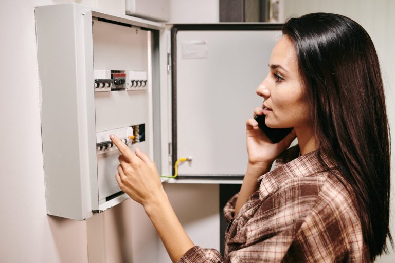 Homeowner on the phone while checking an electrical panel that may need maintenance
